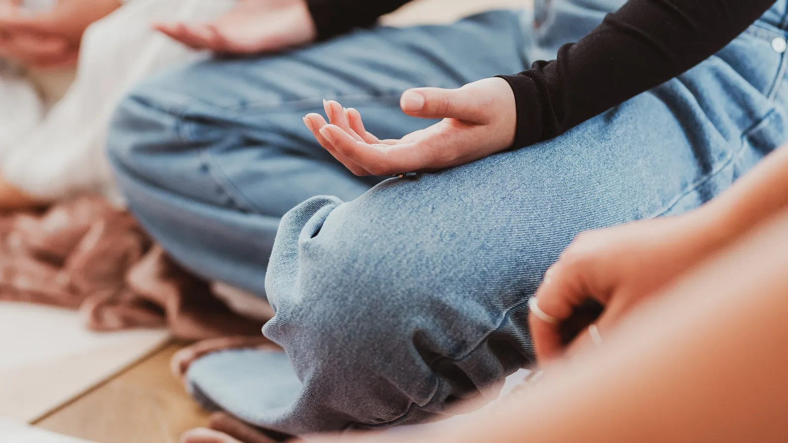 Close-up of hands resting open on crossed knees as a group sits in meditation at Davaar House