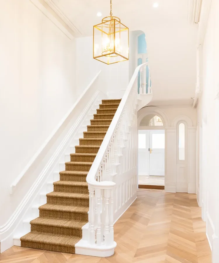 The entrance hall at Davaar House, with its white staircase, brass lantern and herringbone timber floor